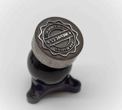 Ein gravierter Metallstempel mit Gravit-Logo steht auf einem dunklen Sockel vor hellem Hintergrund.